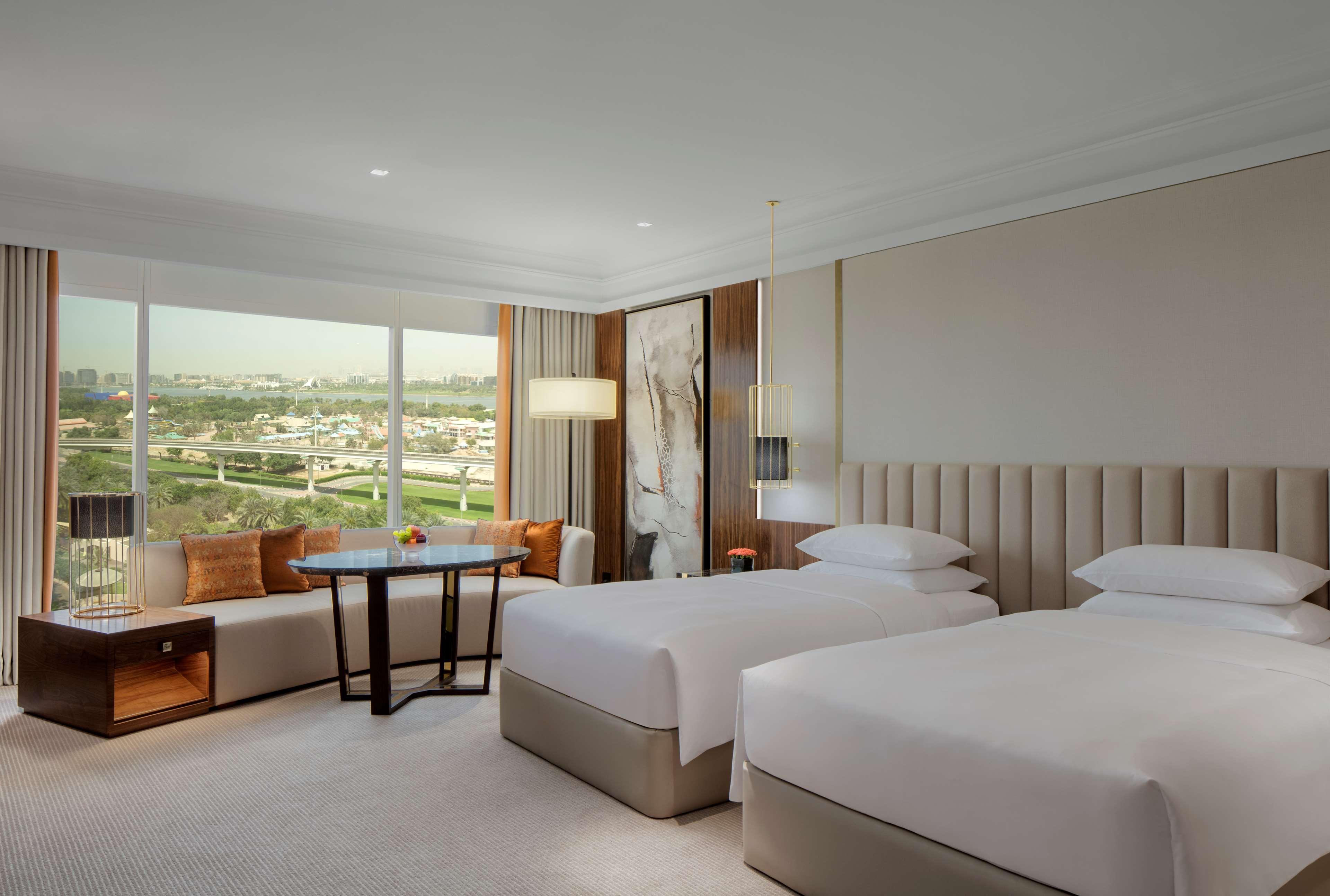 Grand Hyatt Dubai Hotel Ngoại thất bức ảnh The photo shows a modern hotel room featuring two twin beds with white bedding. There is a large window providing a view of the outside landscape, allowing natural light to fill the space. The room is decorated in soft, neutral tones with modern furn