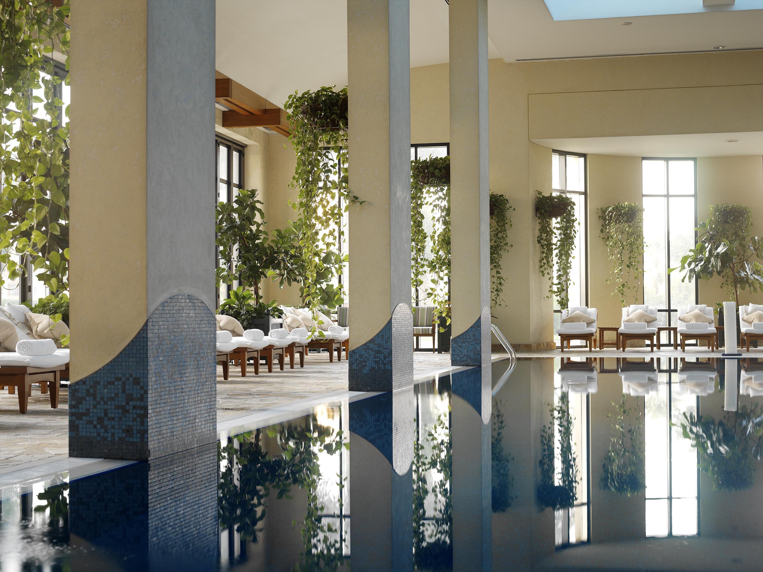 Grand Hyatt Dubai Hotel Tiện nghi bức ảnh The image depicts a serene indoor swimming pool area. It features large windows allowing natural light to stream in, creating a bright and inviting atmosphere. The pool's calm waters reflect the surroundings, including decorative pillars and lush gre