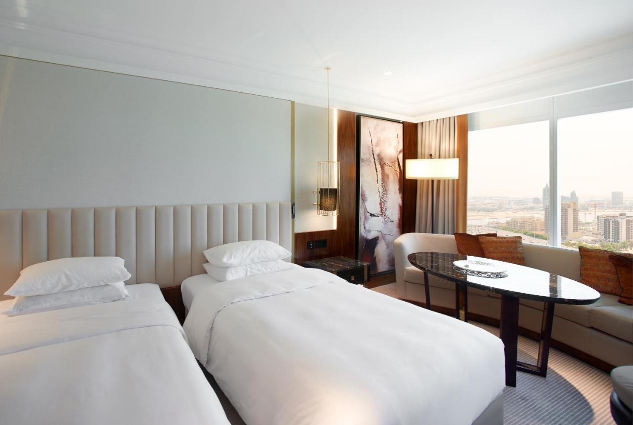Grand Hyatt Dubai Hotel Ngoại thất bức ảnh The photo shows a modern hotel room featuring two separate beds with white bedding. The walls are painted in neutral tones, and there is a large window that allows natural light to enter, offering a view of the city. A stylish round table and chairs 