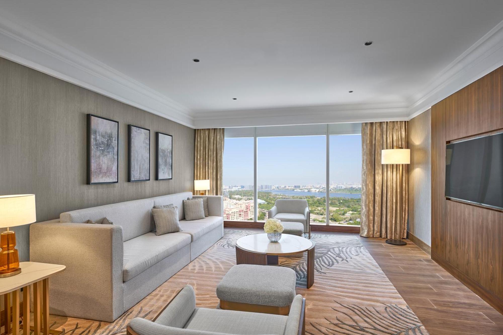 Grand Hyatt Dubai Hotel Ngoại thất bức ảnh The photo shows a modern hotel room featuring a comfortable living area. There is a light-colored sofa with several cushions, a coffee table in the center, and a couple of armchairs. The walls are adorned with framed artworks, and large windows provi