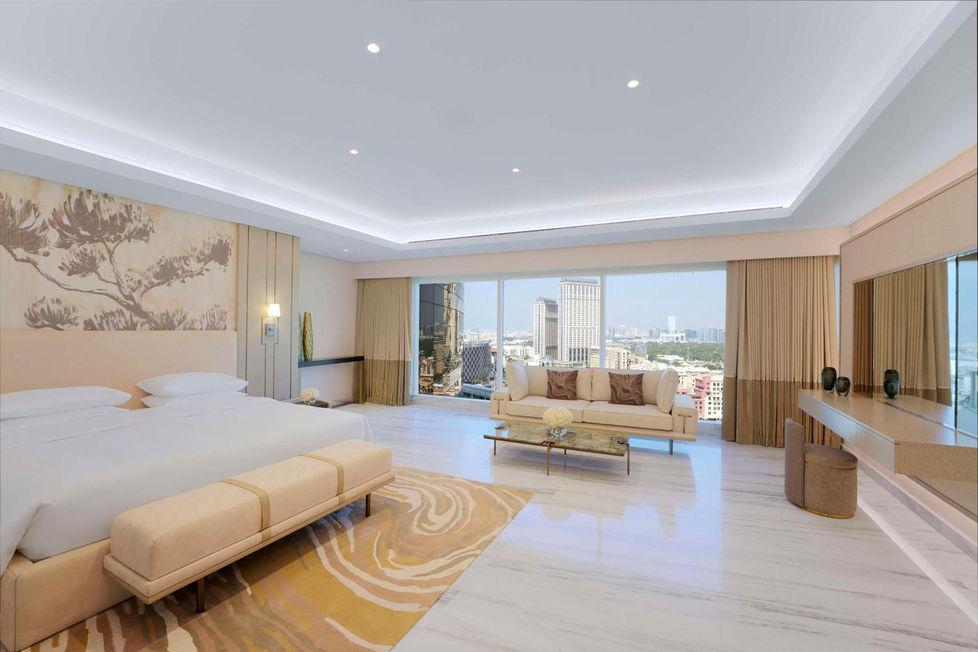 Grand Hyatt Dubai Hotel Ngoại thất bức ảnh The image shows a spacious hotel room that features a contemporary design. It has a large window that offers a view of the city skyline, allowing natural light to fill the space. The room includes a cozy seating area with a light-colored sofa and a s