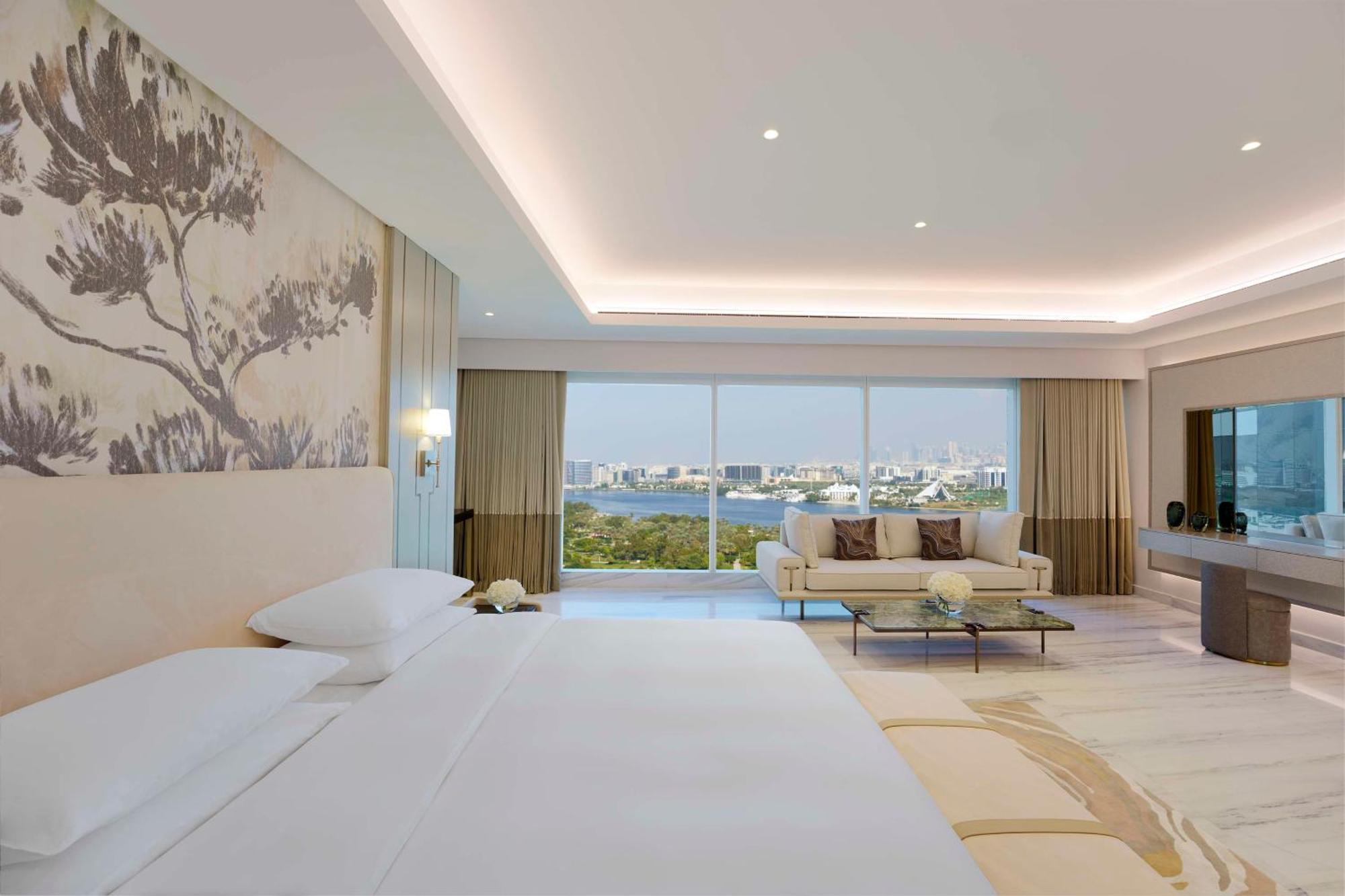 Grand Hyatt Dubai Hotel Ngoại thất bức ảnh The photo depicts a modern hotel room featuring a spacious and elegantly designed interior. There is a large bed with white linens, accompanied by soft pillows. The walls have a subtle decorative element, possibly a mural or wallpaper with natural mo
