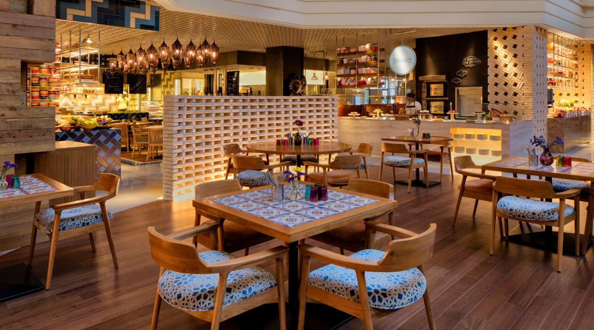 Grand Hyatt Dubai Hotel Ngoại thất bức ảnh The photo shows an elegant restaurant interior. It features wooden flooring and modern decor. The seating is centered around wooden tables with patterned surfaces and comfortable chairs. There are decorative elements, such as vases with colorful flow