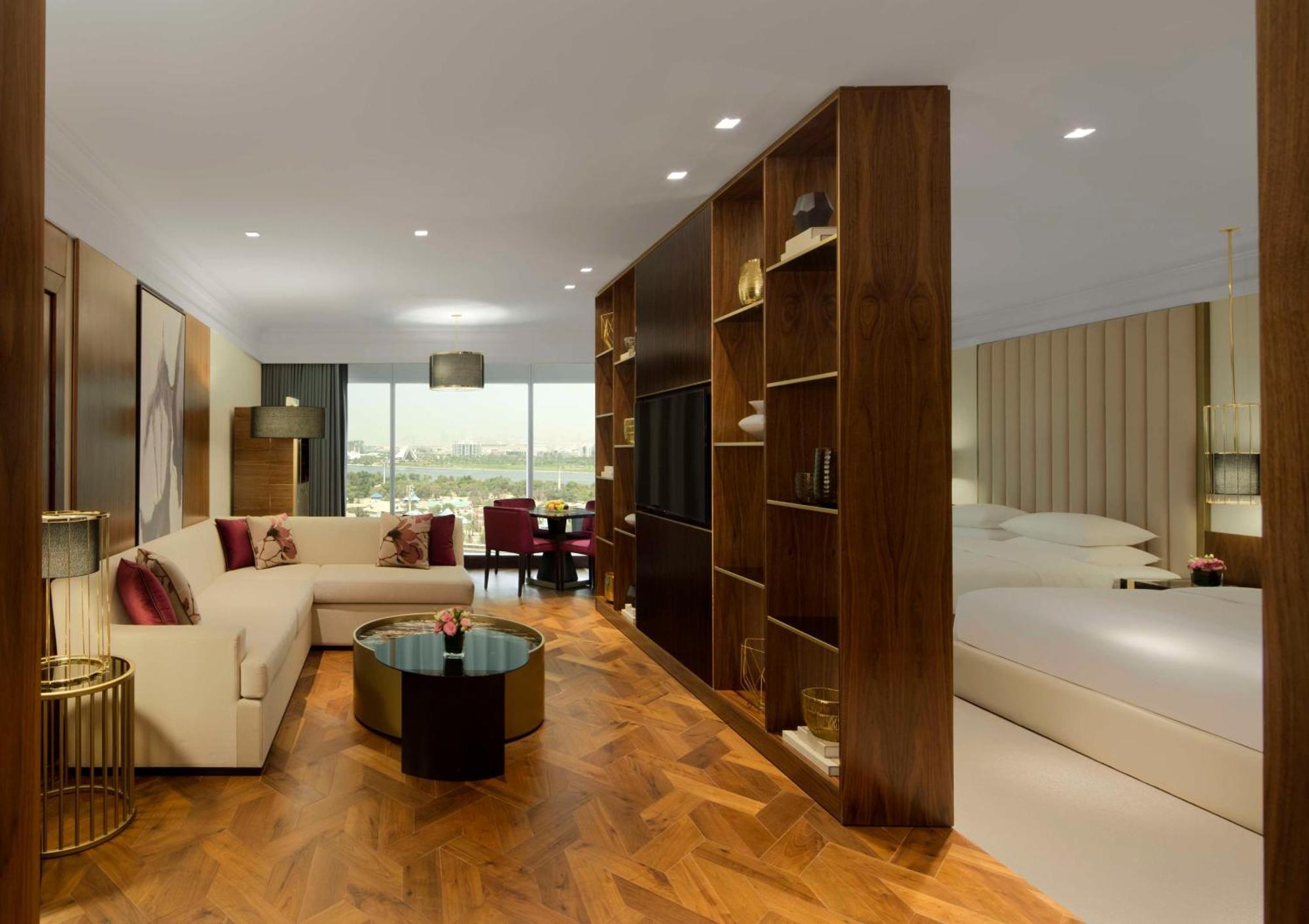 Grand Hyatt Dubai Hotel Ngoại thất bức ảnh The photo shows a modern hotel room designed with a stylish and comfortable aesthetic. On one side, there is a cozy seating area featuring a light-colored sofa with decorative cushions and a small coffee table. In the center of the room, a wooden par