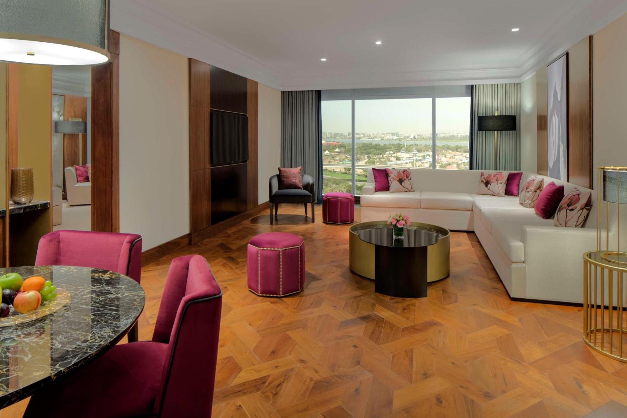 Grand Hyatt Dubai Hotel Ngoại thất bức ảnh The photo shows a modern and stylish living space. There is a large, L-shaped white sofa adorned with pink and purple cushions, complemented by a round black coffee table in the center. In front of the sofa, there are two round ottomans in a matching