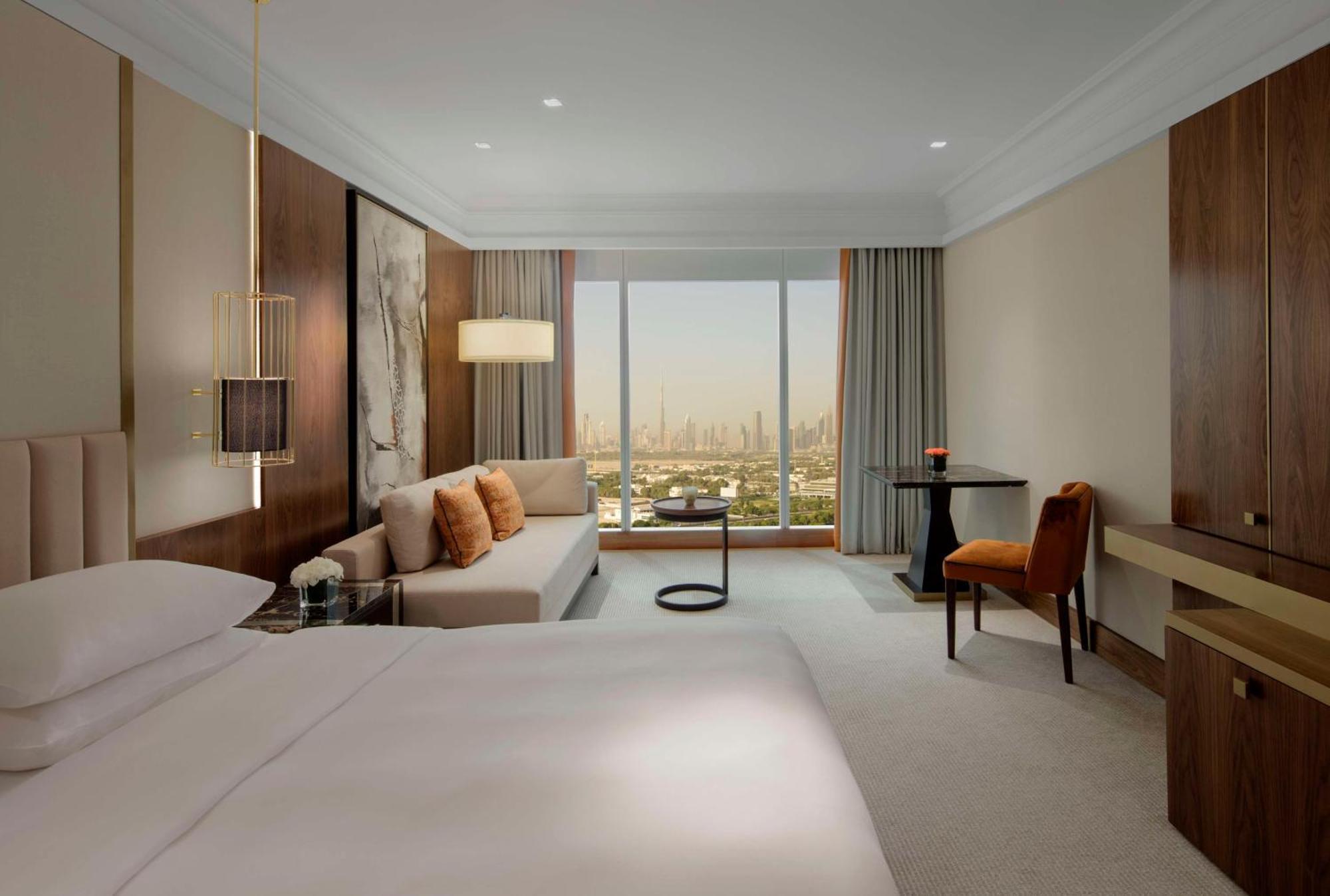 Grand Hyatt Dubai Hotel Ngoại thất bức ảnh The photo shows a modern hotel room with a spacious design. It features a large bed with white linens, a comfortable couch adorned with pillows, and a small round table. A stylish chair sits next to a desk or dresser. The room has large windows offer